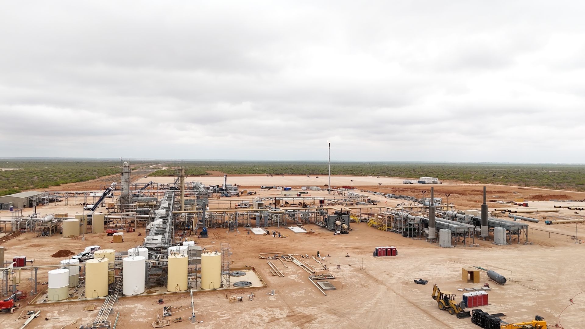 Aerial view of an oil and gas facility in a desert landscape under cloudy skies.